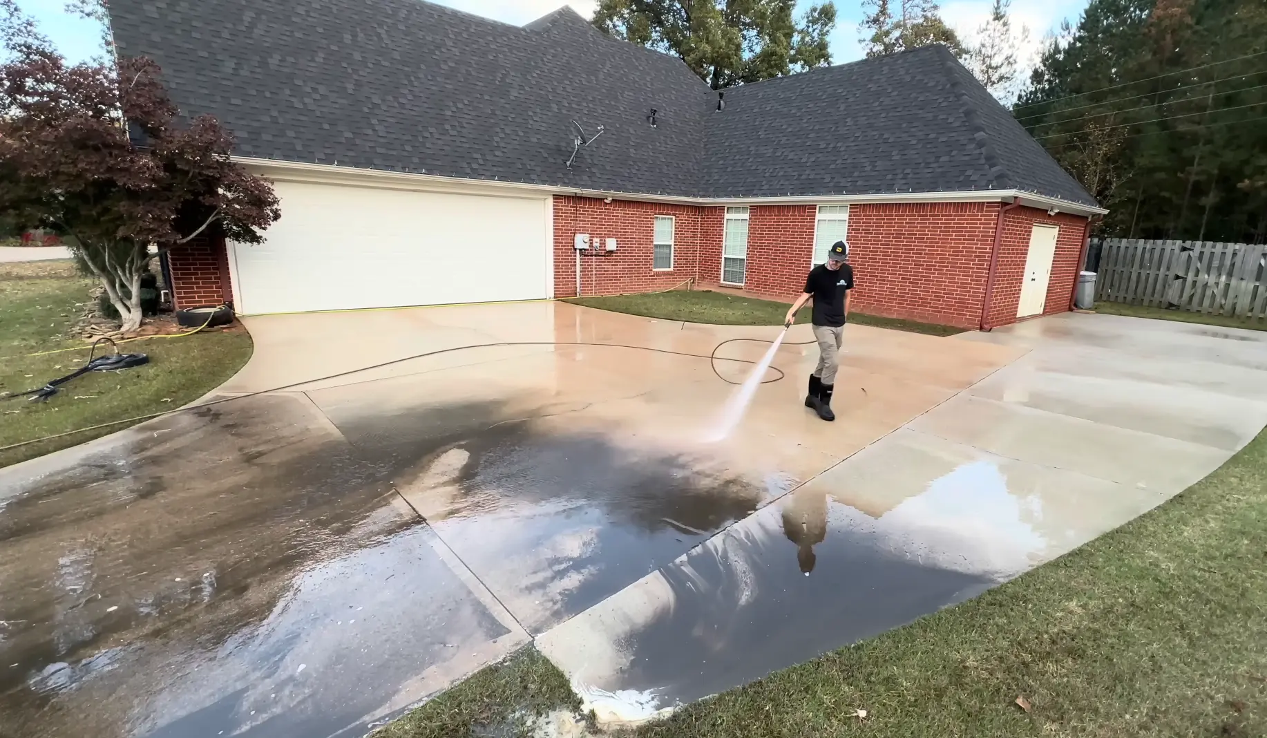 Technician rinsing the concrete driveway of a brick home, the house behind