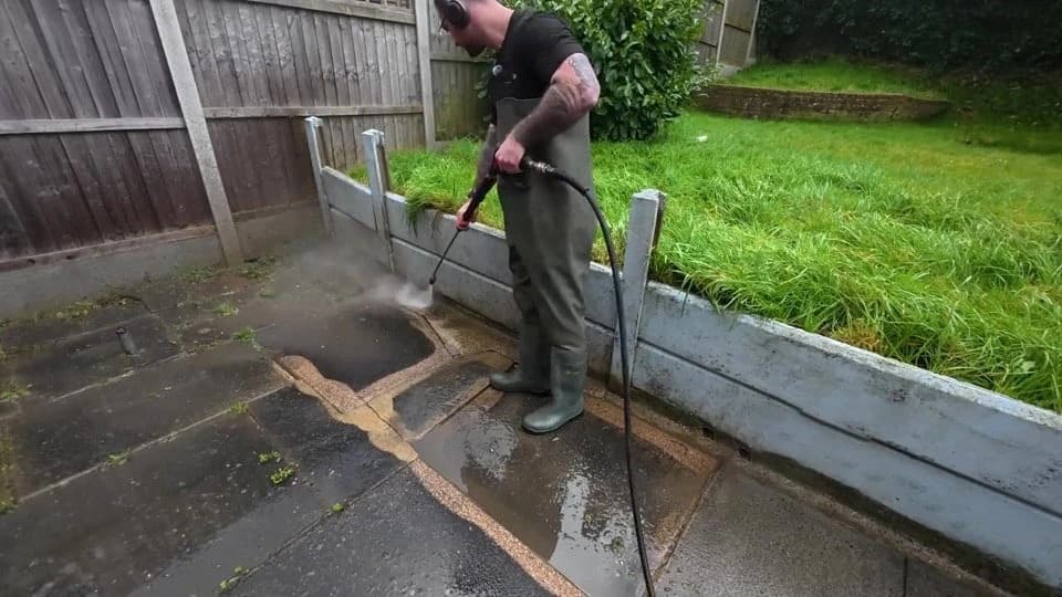 Green algae being washed off a paved patio beside a wooden fence