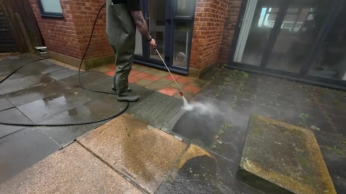Technician washing a paved patio outside the rear door of a brick building