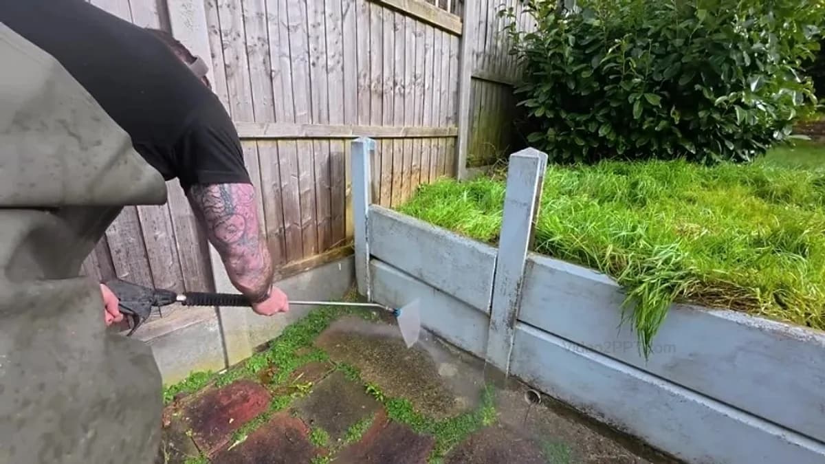 Technician washing the concrete gravel board at the foot of a wooden fence
