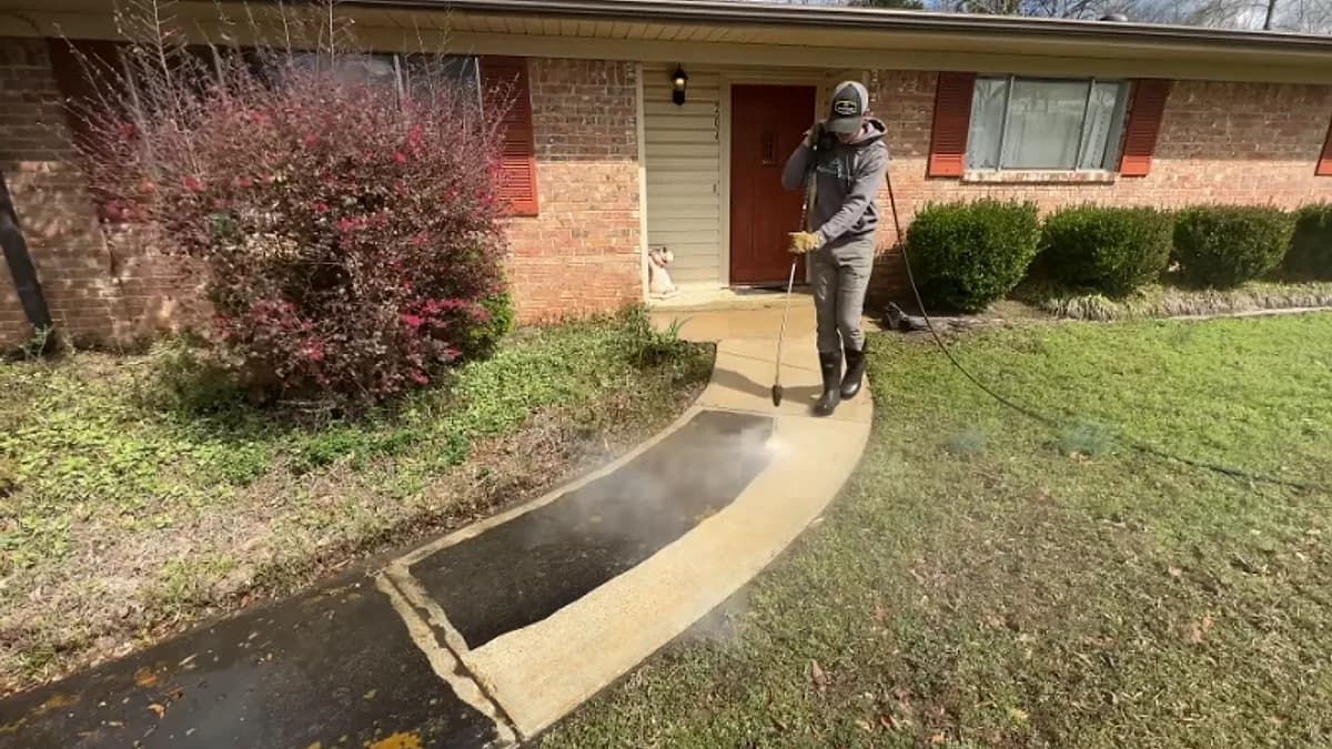 Technician pressure washing the entry walkway of a single-story brick home